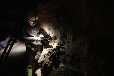EN: Technician working on lighting in a narrow cave passage